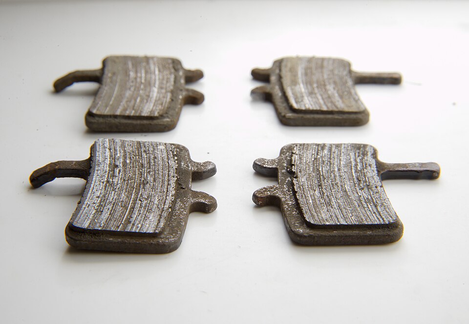 Four worn disc brake pads with scored pad material on metal backing plates